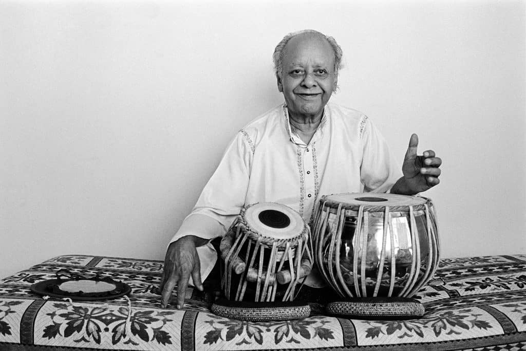 Ustad Alla Rakha sits smiling, with his tabla drums in front of him.