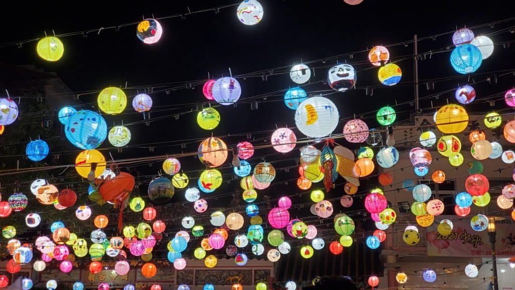 A number of colourful Chinese paper lanterns hung across a street, lit up against the night sky.