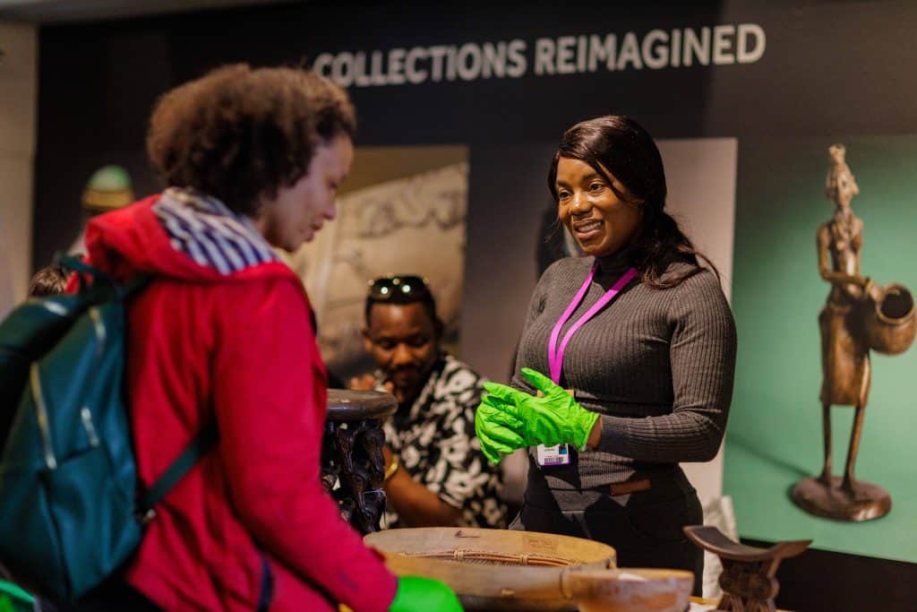 A member of Manchester Museum staff talks to a visitor while allowing them to handle objects from the Museum's African collections.