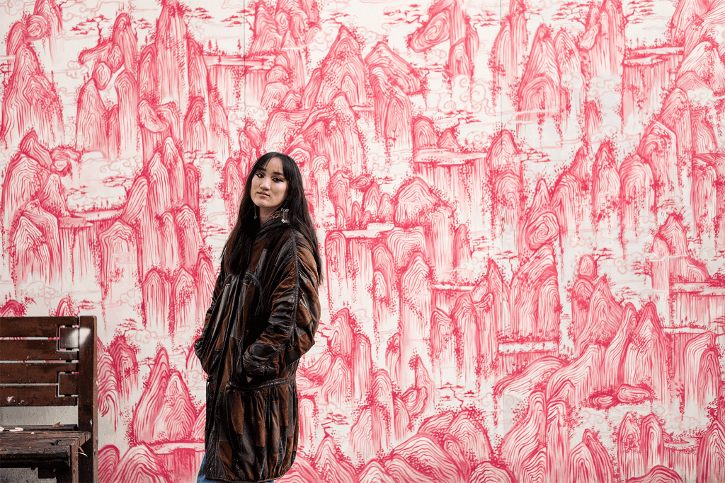 Artist Jasmine Gardner stands in front of a full-wall artwork in red and white.